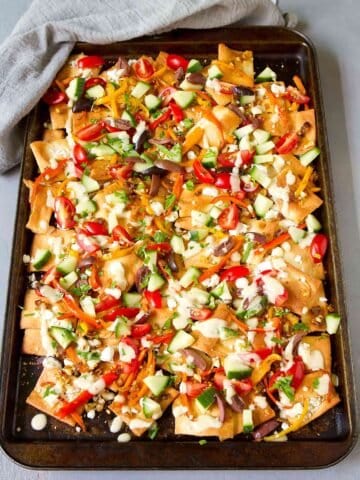 Baking sheet with nachos. With goat cheese, tomatoes, cucumber, peppers and hummus dressing.