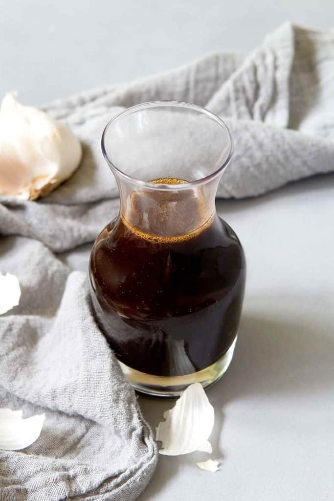 Glass carafe with balsamic vinaigrette, on a gray background with a napkin and garlic cloves.