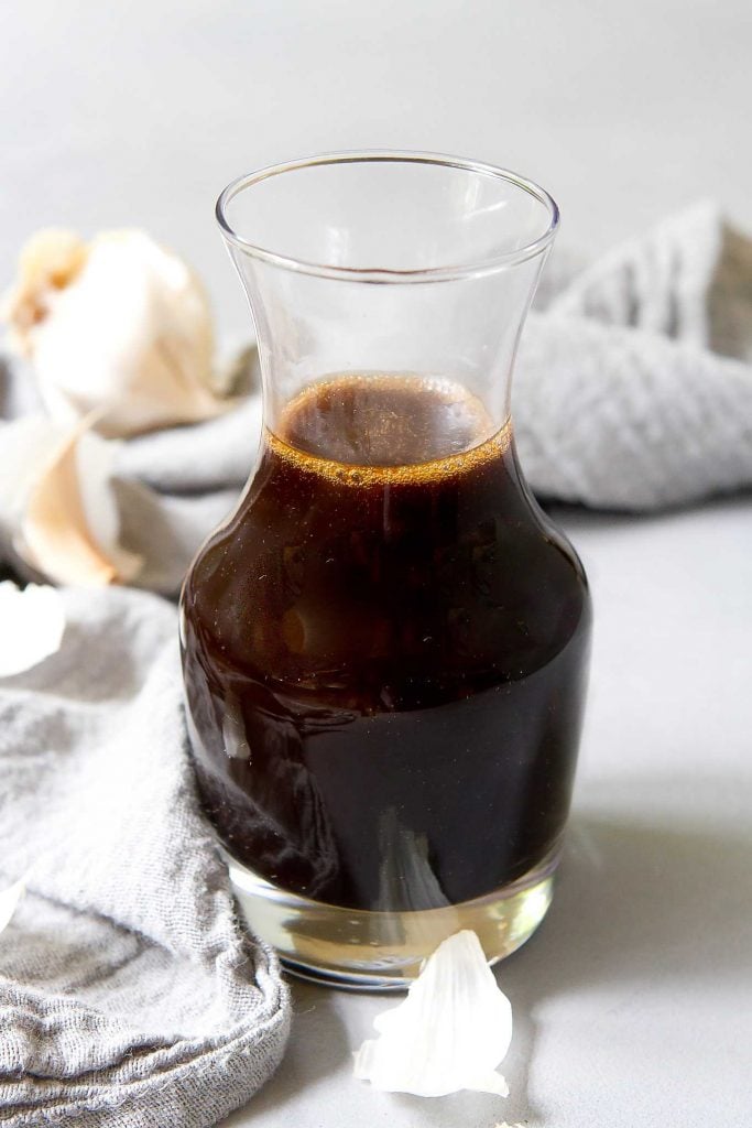 Easy balsamic dressing in a glass carafe, with a gray napkin and cloves of garlic.