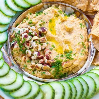 Roasted cauliflower dip with chopped pecans and parsley, surrounded by cucumber slices.
