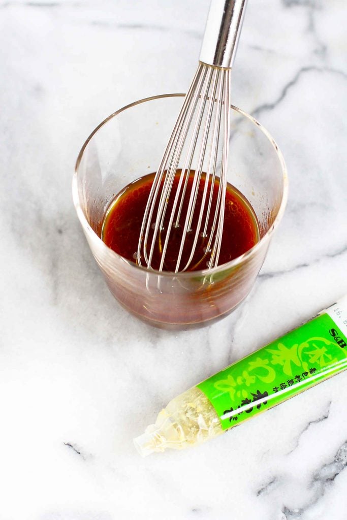 Soy sauce dressing in a glass with a whisk. Tube of wasabi paste on the side.