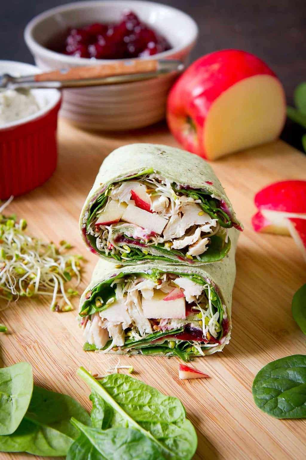 Turkey, cranberry and vegetable wrap sandwich. Apple, broccoli sprouts and bowls in the background.