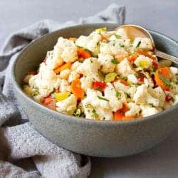 Cauliflower salad with chopped pepperoncini and roasted peppers in a dark gray bowl.