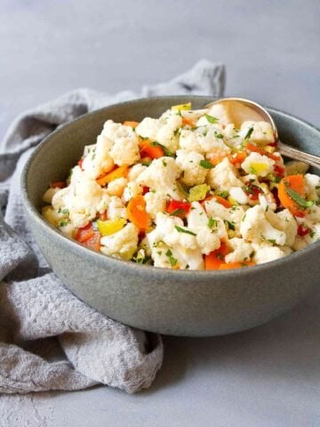 Cauliflower salad with chopped pepperoncini and roasted peppers in a dark gray bowl.