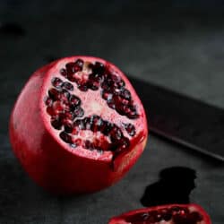 Pomegranate with one side cut off, seeds exposed, with black background.