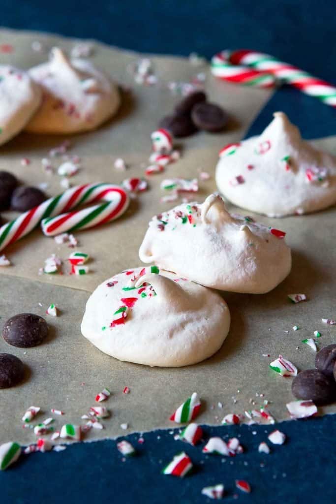 Several meringue cookies on parchment paper, surrounded by some mini candy canes and chocolate chips