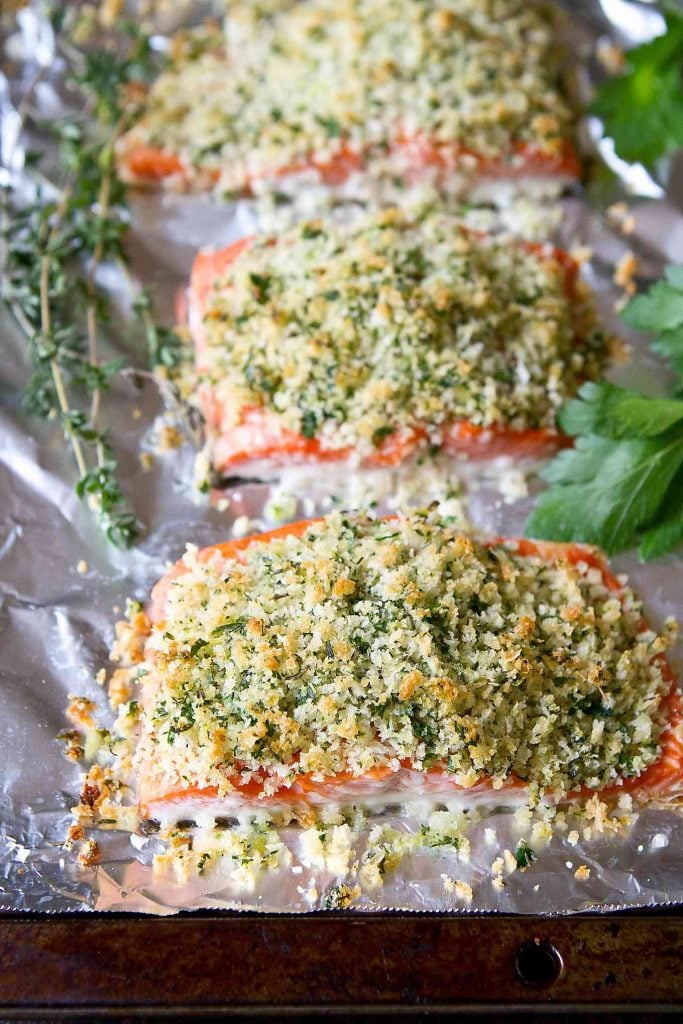 Salmon fillets on a foil-lined baking sheet, topped with a Parmesan cheese, herb and breadcrumb topping.