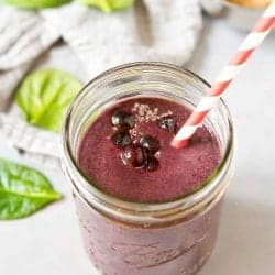 Blueberry banana smoothie in a mason jar, surrounded by spinach and banana.