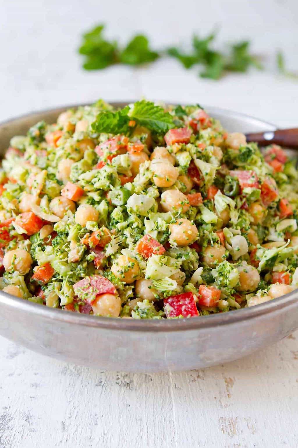 Chopped broccoli salad with chickpeas and other vegetables in a silver bowl.