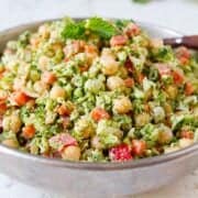 Chopped broccoli salad with chickpeas and other vegetables in a silver bowl.