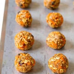 No-bake energy bites filled with shredded carrots and raisins, lined up on baking sheet.