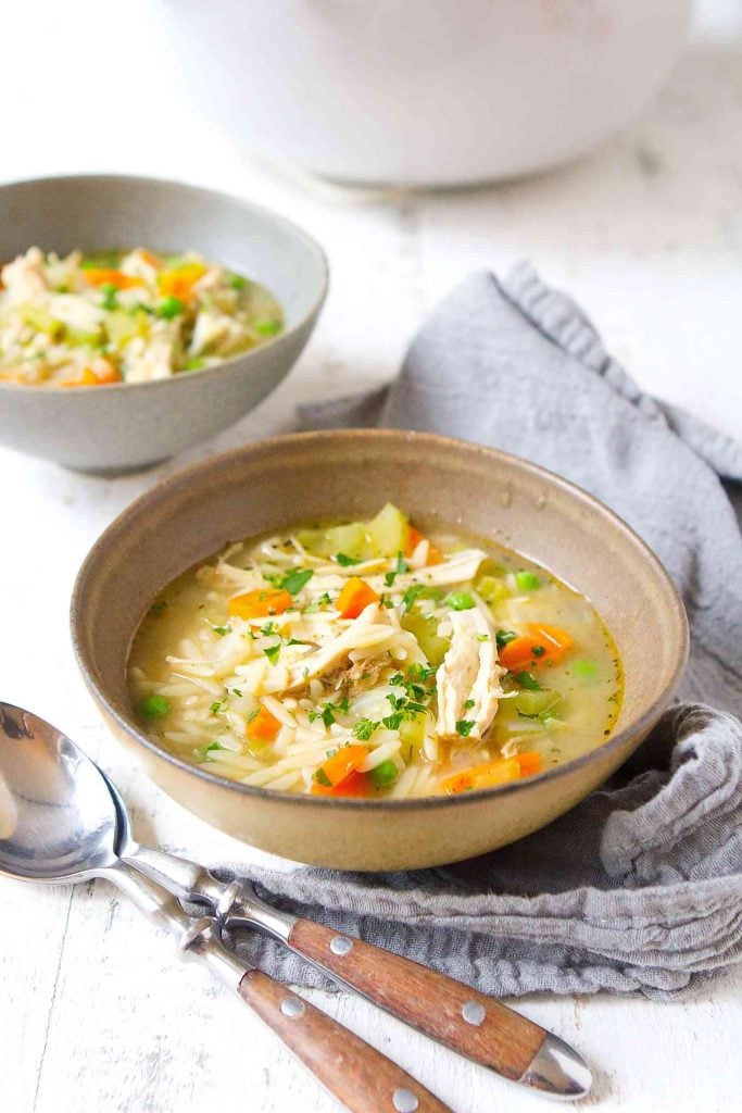  Chicken and vegetable soup in light brown and gray bowls, on gray napkin.