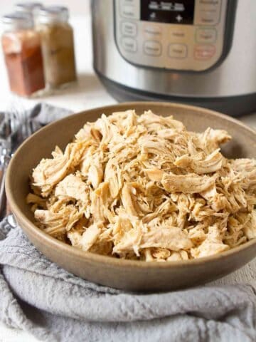 Shredded chicken in a brown bowl, with Instant Pot in background.
