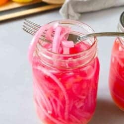 Jar of pickled red onions, with orange, lemon and lime peels in background.