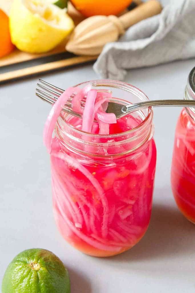Jar of pickled red onions, with orange, lemon and lime peels in background.