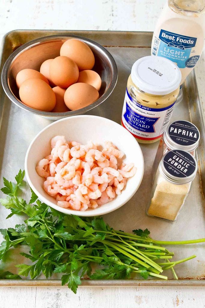 Hard boiled eggs, shrimp, mayonnaise, mustard, parsley, paprika and garlic powder on a baking sheet.