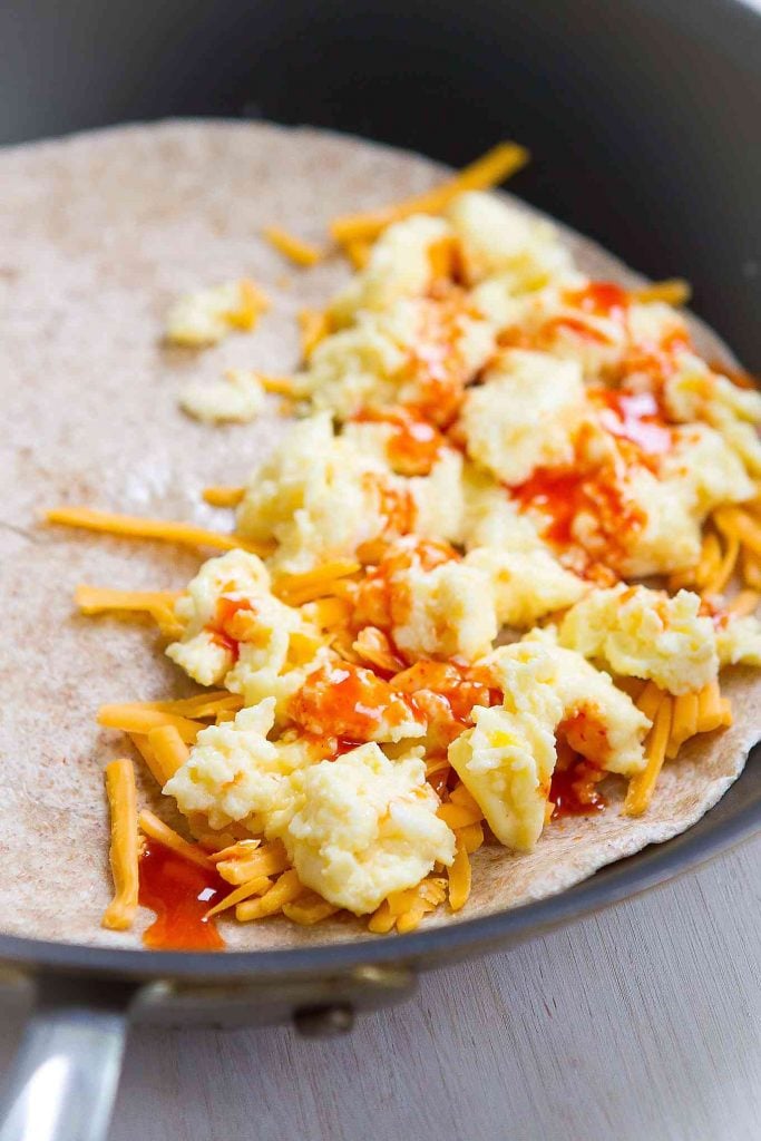 Scrambled eggs, cheese & hot sauce on a tortilla, in a skillet.