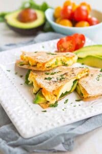 Quesadilla, but in wedges, filled with egg, avocado and spinach on a white plate.
