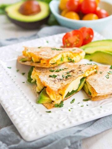 Quesadilla, but in wedges, filled with egg, avocado and spinach on a white plate.