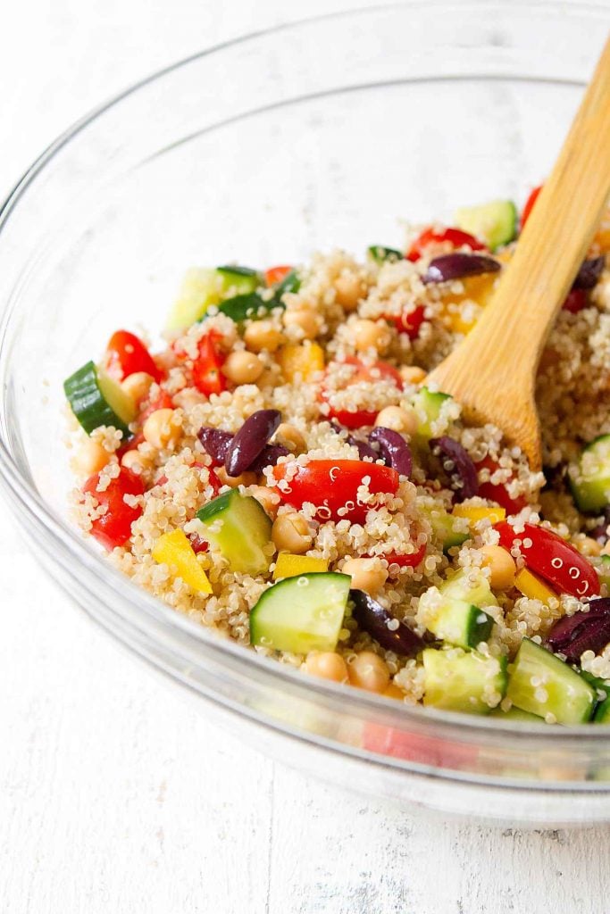 Quinoa chickpea salad with vegetables in a glass bowl with wooden spatula.