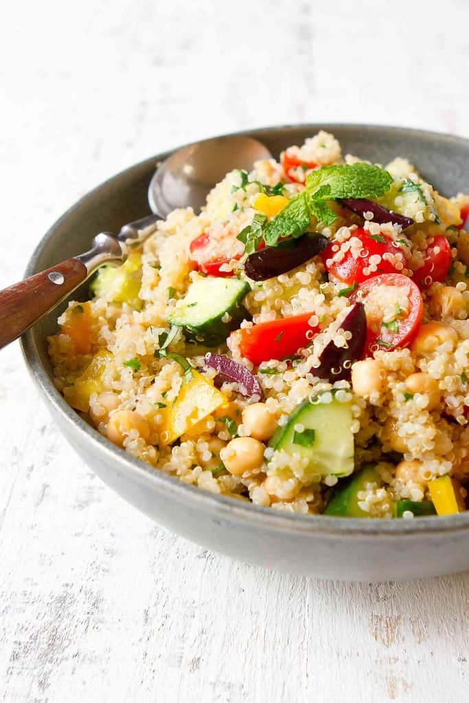 Quinoa salad with tomato, cucumber, bell pepper, herbs and olives in a gray bowl.
