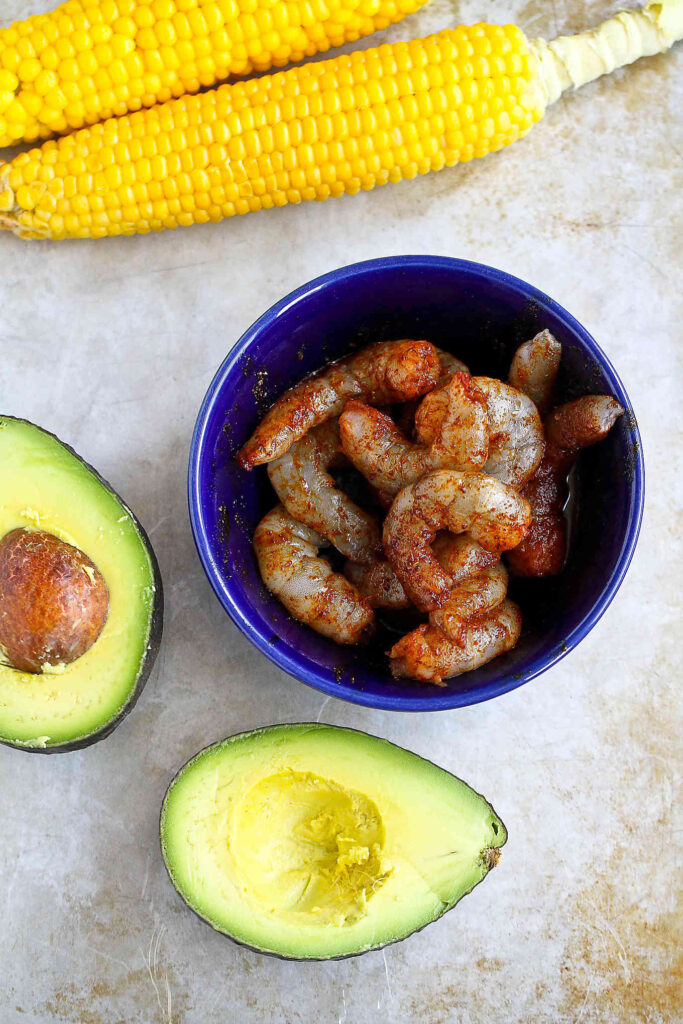 Spiced shrimp in a blue bowl, avocado and ear of corn.