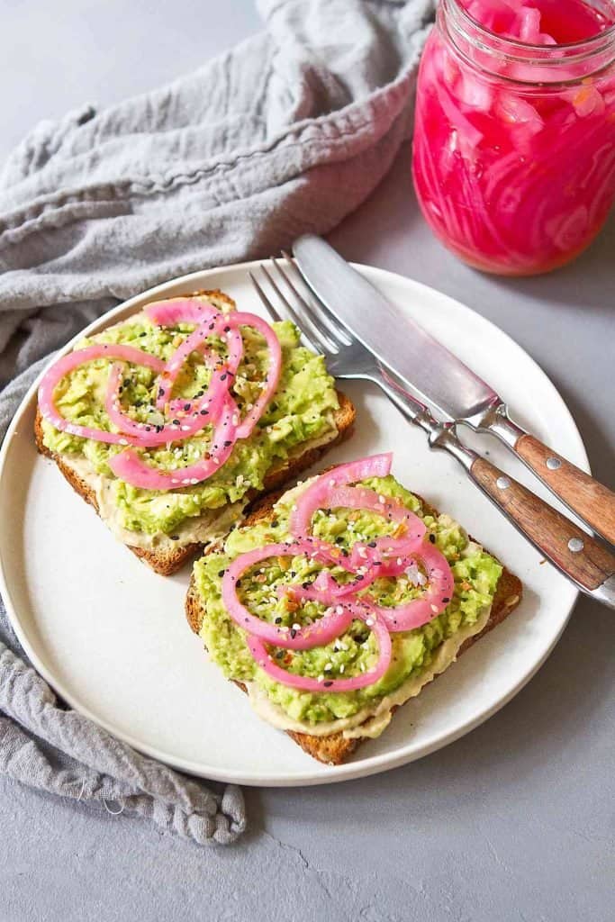 Two pieces of avocado toast topped with red onions on a white plate.