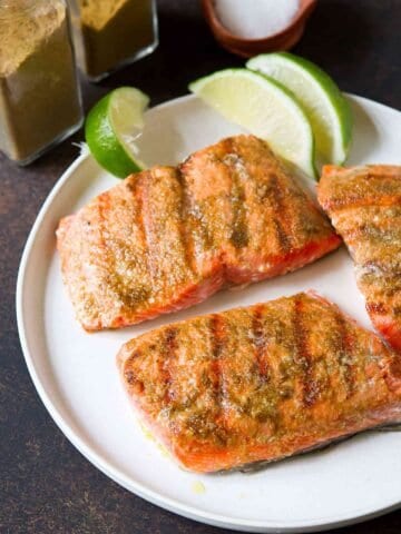 Pieces of grilled salmon and lime wedges on a white plate.