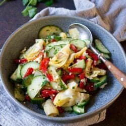 Salad with cucumber, roasted red pepper, artichokes and feta in a gray bowl.