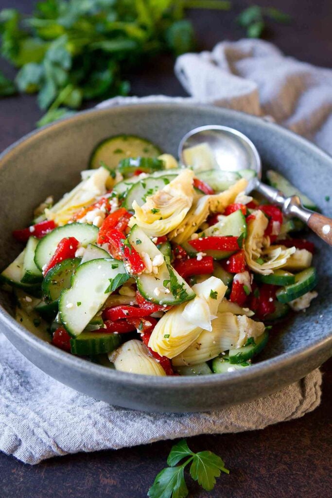 Mediterranean cucumber salad, with roasted peppers and artichokes in a gray bowl.