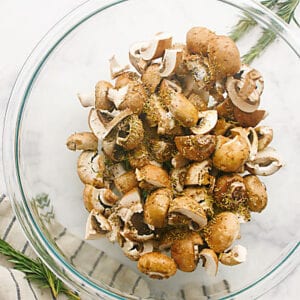 Mushroom pieces in a glass bowl with olive oil and rosemary.