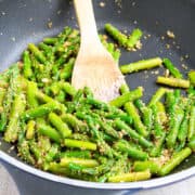 Sauteed asparagus, mixed with garlicky breadcrumbs, in a black skillet.