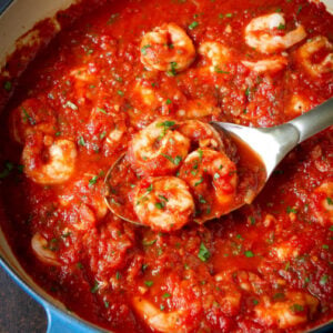 Shrimp in red sauce with stainless steel spoon in skillet.
