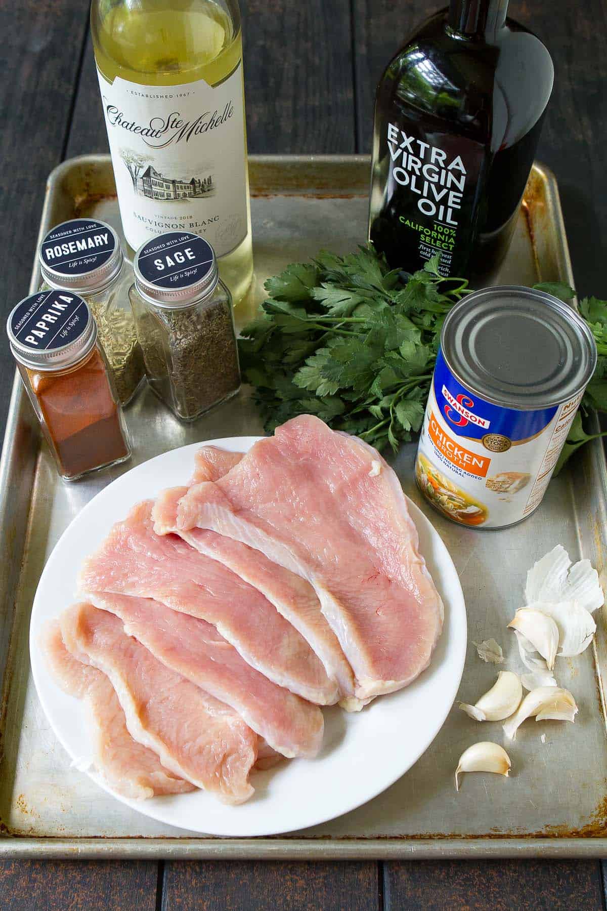 Turkey cutlets, spices, wine, broth and garlic on a baking sheet.