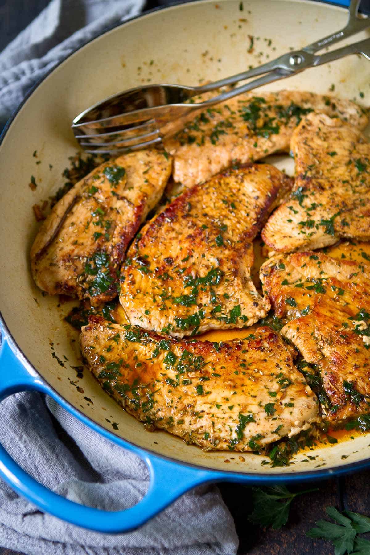 Cooked turkey breast fillets with wine sauce in blue skillet.