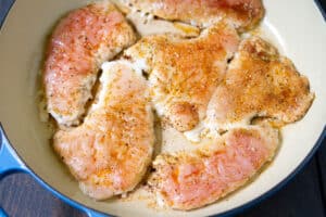 Partially cooked turkey cutlets in a large skillet.