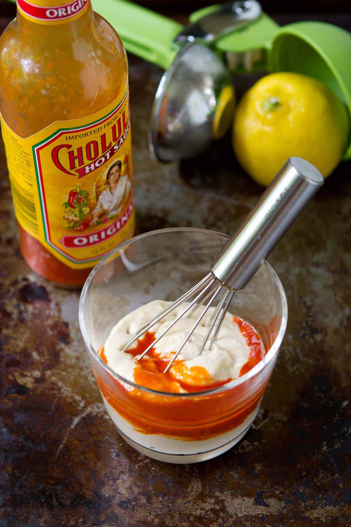 Hummus and hot sauce in a glass. Lemon and hot sauce in background.