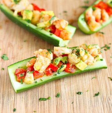 Shrimp and avocado mixture in cucumber boats, all on wooden cutting board.