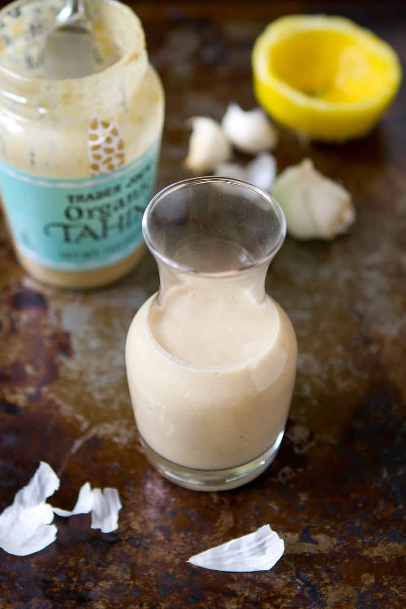 Tahini dressing in small glass carafe. Jar of tahini and lemon.