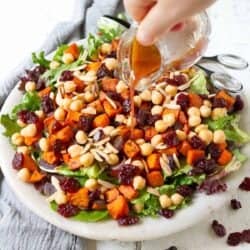 Pouring dressing over salad with sweet potato, tart cherries, greens and chickpeas.