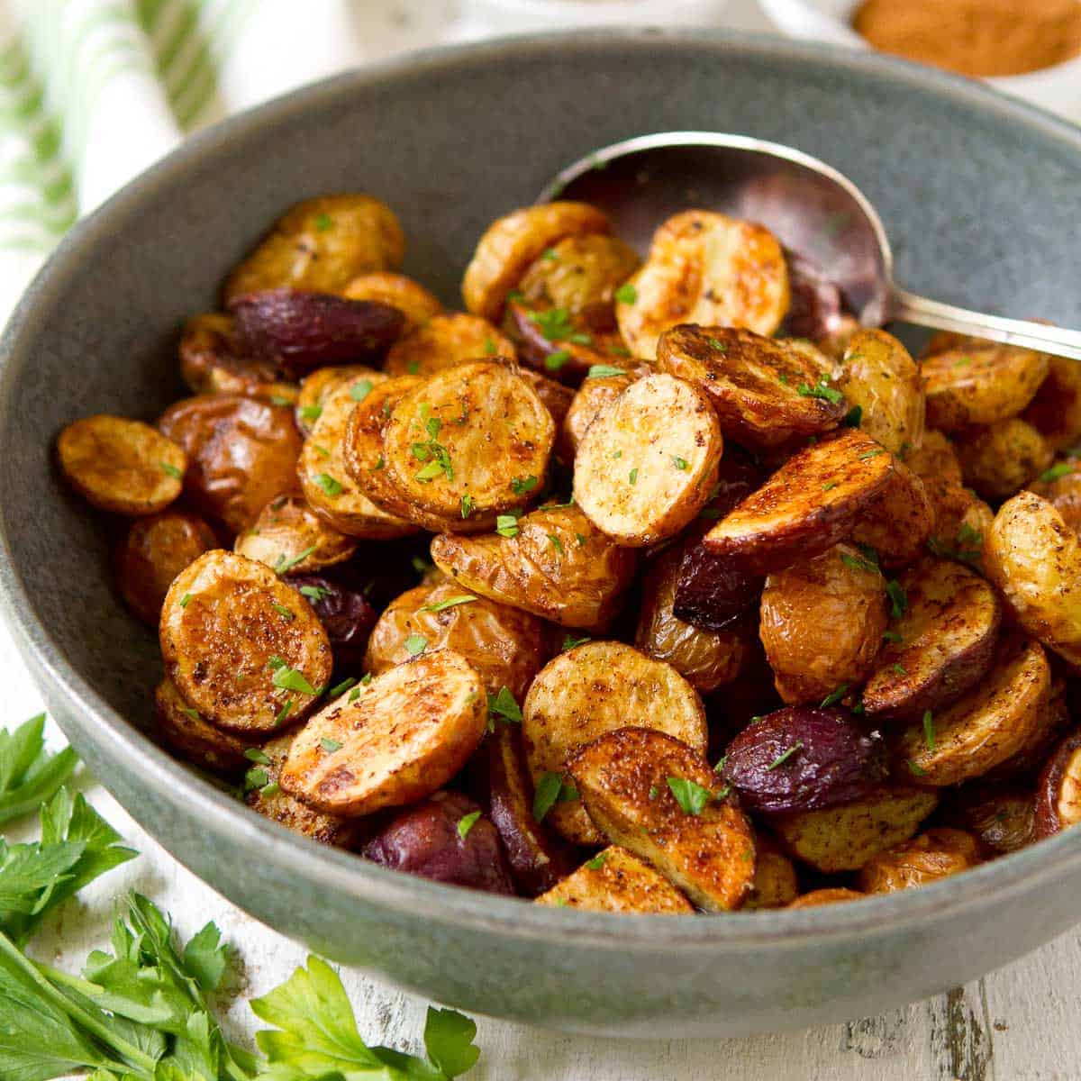 Roasted potatoes in a gray bowl, seasonings in small bowls.