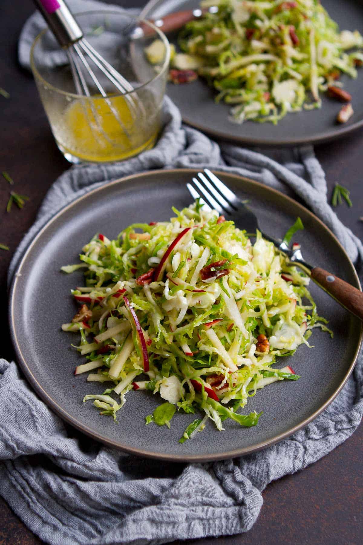 Gray plates with slaw of Brussels sprouts, apple and nuts, with fork on the side.