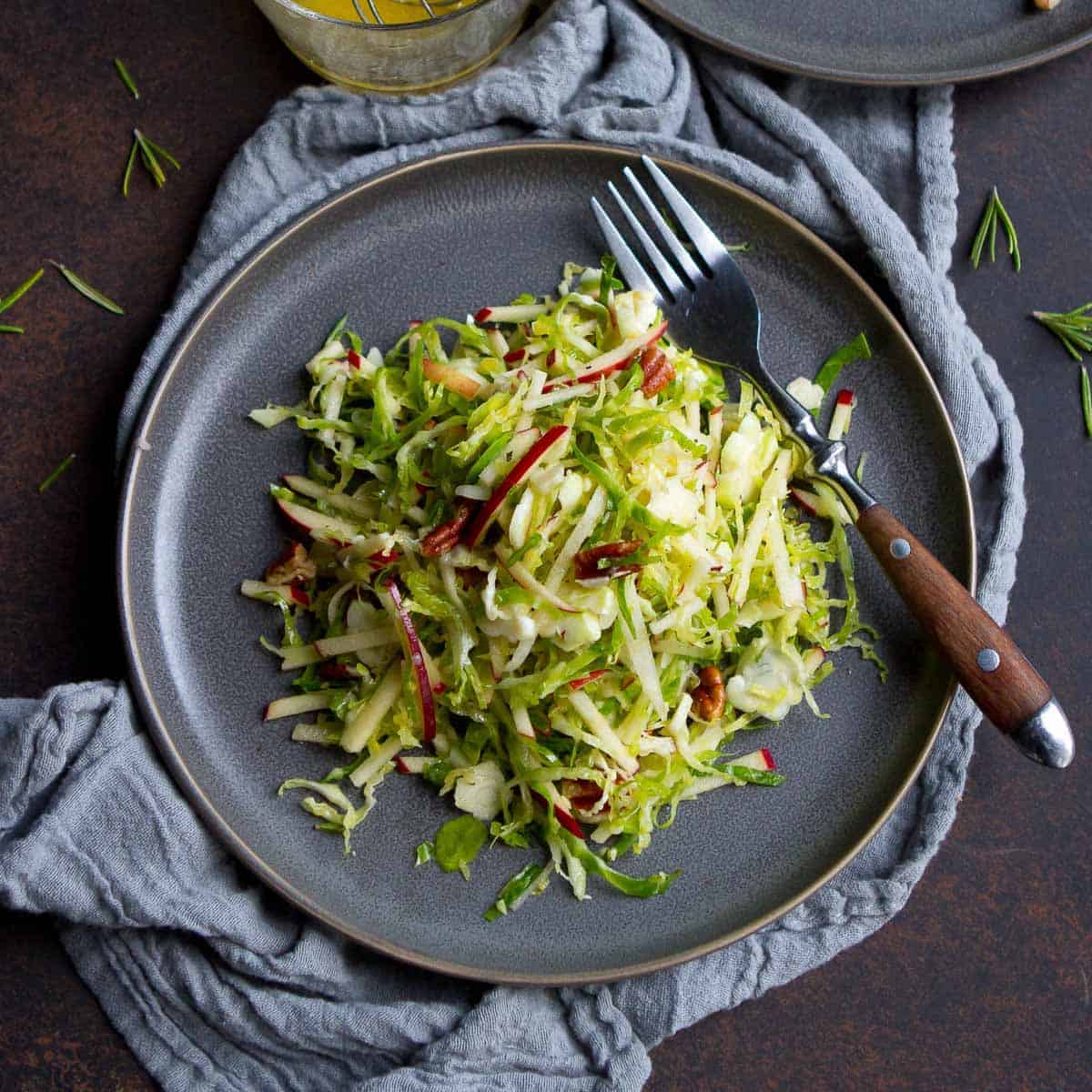 Apple and shredded Brussels sprouts slaw on gray plates, with gray napkin.