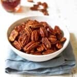 Maple pecans in a white bowl, sitting on a blue napkin.