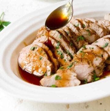 Sliced pork tenderloin on a white plate. Spoon drizzling glaze over top.