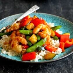 Shrimp stir fry with vegetables on a blue plate and a white plate.