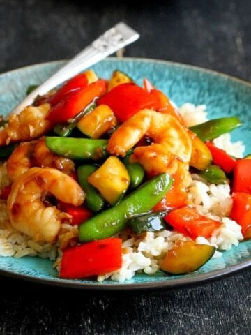 Shrimp stir fry with vegetables on a blue plate and a white plate.