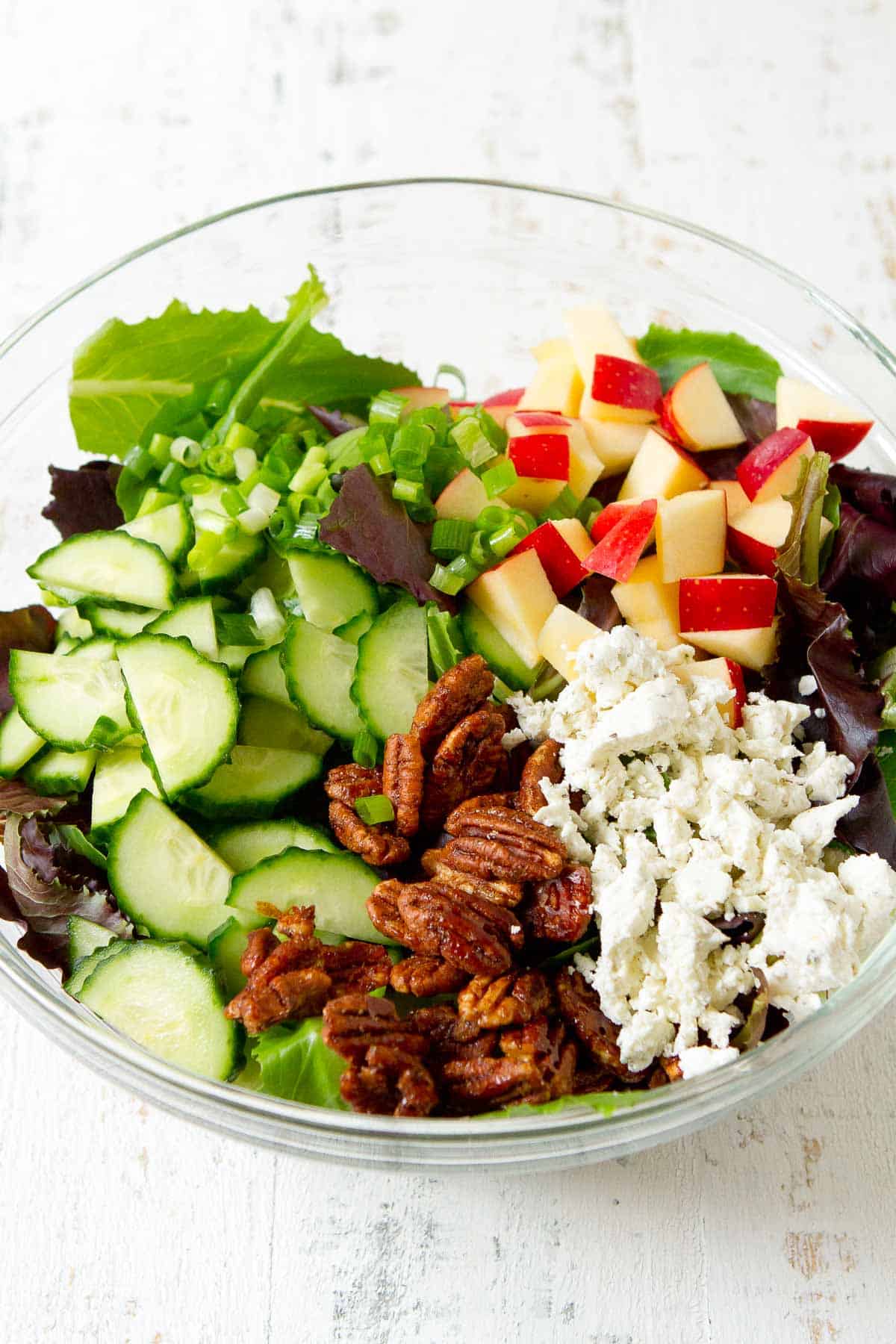 Green, cucumber, apple, pecans and goat cheese in a glass bowl.