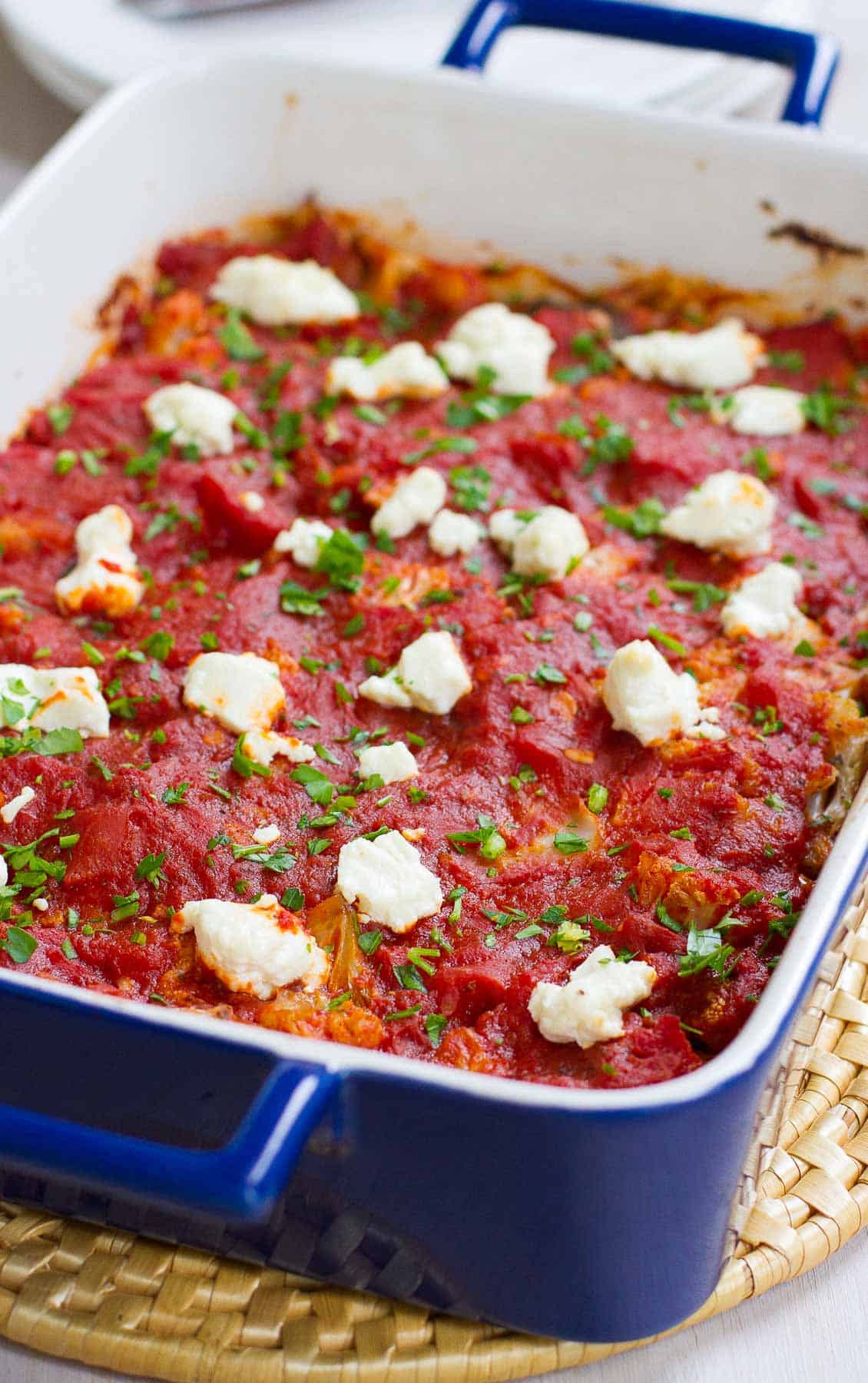 Blue casserole dish with cauliflower, tomato sauce and goat cheese.