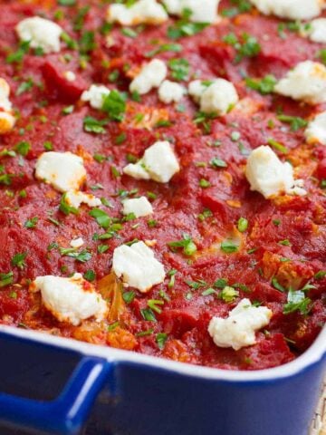 Blue casserole dish with cauliflower, tomato sauce and goat cheese.
